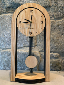 This shows an pendulum clock with a a round top  above two straight legs of the clock, with a pendulum swinging in the middle. The motif is Walnut against black. The style is a solid-modern look with a mission-style pendulum and sides. 