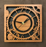 Square walnut clock with black background. The front shows a large single gear surrounded by smaller gears and partial gears, and the numbers 12, 3 , 6, 9. One layer down are two smaller gears. 8" size