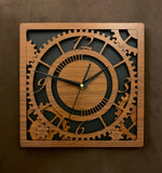 Square walnut clock with black background. The front shows a large single gear surrounded by smaller gears and partial gears, and the numbers 12, 3 , 6, 9. One layer down are two smaller gears. Larger sizes