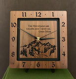 A square walnut clock with the numbers on the outer square section, while on the inner square section a mountain and the words, "The Mountains are calling and I must go. -John Muir" are lasered in the wood. The concentric wood squares have a gap between them and are against a black background. 8" Size on easel