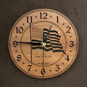 Larger sizes of the round Walnut clock with a laser-cut flag in the middle, the words, "Land of the Free" beneath it, surrounded by a circular cut-out band showing the black background, and the numbers 1-12 cut through around the perimeter.