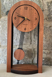This shows a pendulum clock with a round top  above two straight legs of the clock, with a pendulum swinging in the middle. The motif is Walnut against black. The style is a solid-modern look with a mission-style pendulum and sides. This is the large size.