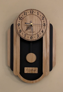 Oblong oak and black pendulum clock consisting of a round face and, under it to either side, 3 alternating oak and black rounded segments which decrease in size from front to back. The clock has a rounded bottom and a black background beneath the face. Front view, smaller sizes