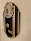 Oblong oak and black pendulum clock consisting of a round face and, under it to either side, 3 alternating oak and black rounded segments which decrease in size from front to back. The clock has a rounded bottom and a black background beneath the face. View seen from angled front.