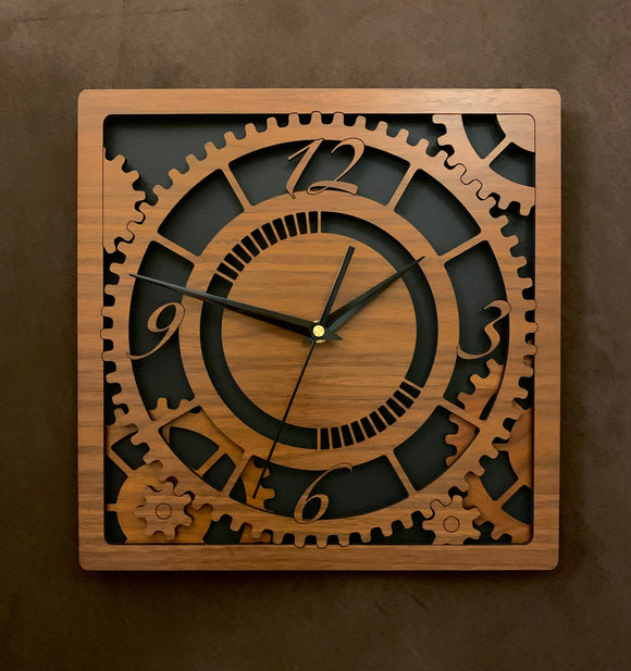 Square walnut clock with black background. The front shows a large single gear surrounded by smaller gears and partial gears, and the numbers 12, 3 , 6, 9. One layer down are two smaller gears. Larger sizes
