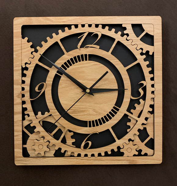 Square oak clock with black background. The front shows a large single gear surrounded by smaller gears and partial gears, and the numbers 12, 3 , 6, 9. One layer down are two smaller gears. Larger sizes