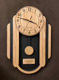 Oblong oak and black pendulum clock consisting of a round face and, under it to either side, 3 alternating oak and black rounded segments which decrease in size from front to back. The clock has a rounded bottom and a black background beneath the face. Front view medium size