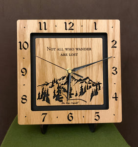 A square oak clock with the numbers on the outer square section, while on the inner square section a mountain and the words, "Not All Who Wander Are Lost" are lasered in the wood. The concentric wood squares have a gap between them and are against a black background. Larger Sizes