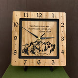 A square oak clock with the numbers on the outer square section, while on the inner square section a mountain and the words, "The Mountains are calling and I must go. -John Muir" are lasered in the wood. The concentric wood squares have a gap between them and are against a black background. 8" Size on easel