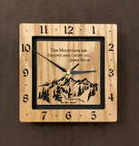 A square oak clock with the numbers on the outer square section, while on the inner square section a mountain and the words, "The Mountains are calling and I must go. -John Muir" are lasered in the wood. The concentric wood squares have a gap between them and are against a black background. 8" Size