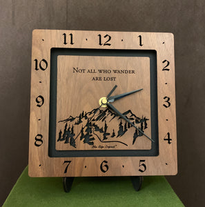 A square walnut clock with the numbers on the outer square section, while on the inner square section a mountain and the words, "Not All Who Wander Are Lost" are lasered in the wood. The concentric wood squares have a gap between them and are against a black background. Larger Sizes