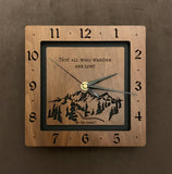 A square walnut clock with the numbers on the outer square section, while on the inner square section a mountain and the words, "Not All Who Wander Are Lost" are lasered in the wood. The concentric wood squares have a gap between them and are against a black background. 8" Size