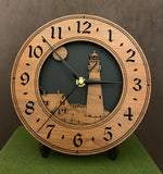 Round oak clock with a lighthouse, moon and lightkeeper's house lasered in the face against a black background - 8" on easel