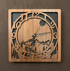 A walnut square clock with two concentric  circles on front with the numbers 1-12, the second level shows a cutout mountain with a moon above, all set against a black background. 