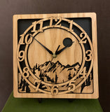 An oak square clock with two concentric  circles on front with the numbers 1-12, the second level shows a cutout mountain with a moon above, all set against a black background. 8" Size shown on easel
