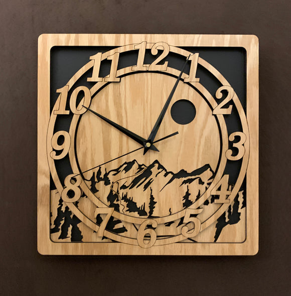 An oak square clock with two concentric circles on front with the numbers 1-12, the second level shows a cutout mountain with a moon above, all set against a black background. Larger sizes