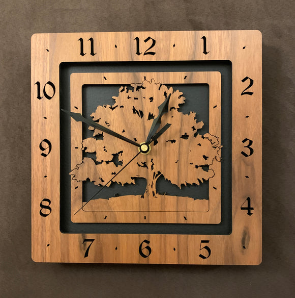 A square walnut clock with the numbers on the outer square section, while a tree is lasered into the inner square section. The concentric wood squares have a gap between them and are set against a black background.